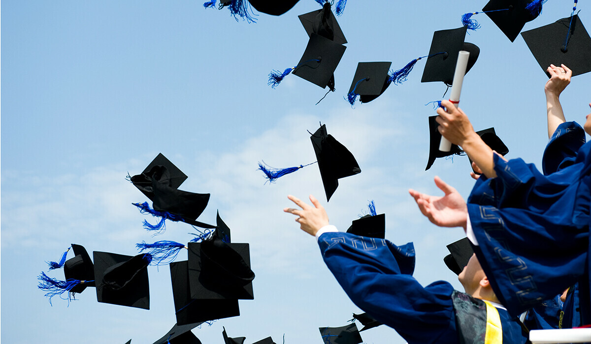 Students toss graduation caps into the air against a blue sky.