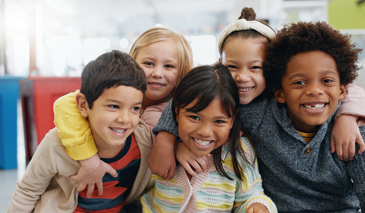 A group of five diverse children facing the camera. They are smiling and have their arms around one another.